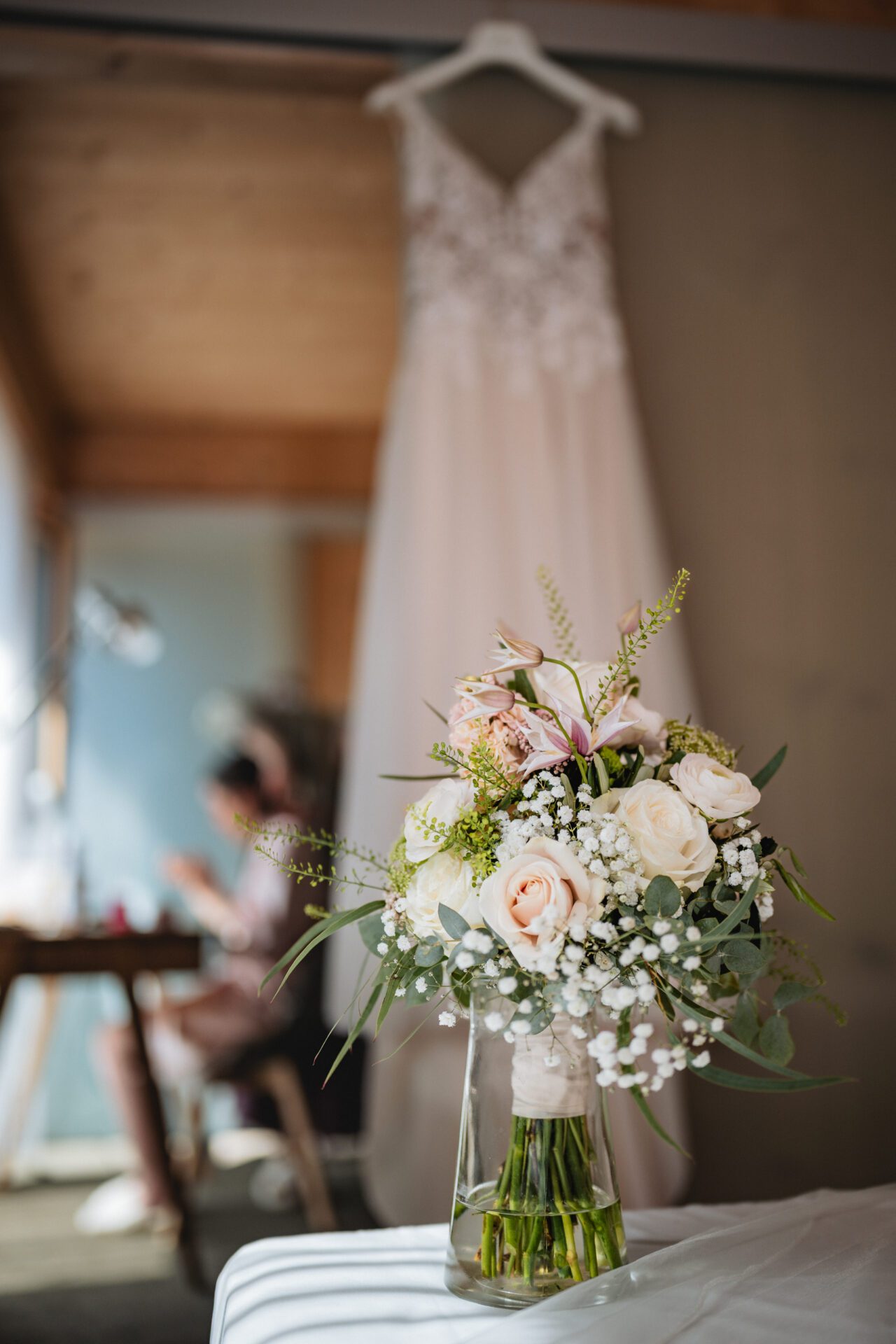 Bei einer formellen Veranstaltung in München beugt sich ein Mann in Hosenträgern vor, um mit einem Gast im Anzug zu sprechen, während eine Frau in der Nähe nach unten schaut. Elegant gedeckte Tische und Blumenarrangements bilden die Kulisse, die ein Hochzeitsfotograf inmitten der sich unter die Gäste mischenden Gäste wunderschön eingefangen hat. Hochzeitsfotos_Hochzeitsfotograf_München