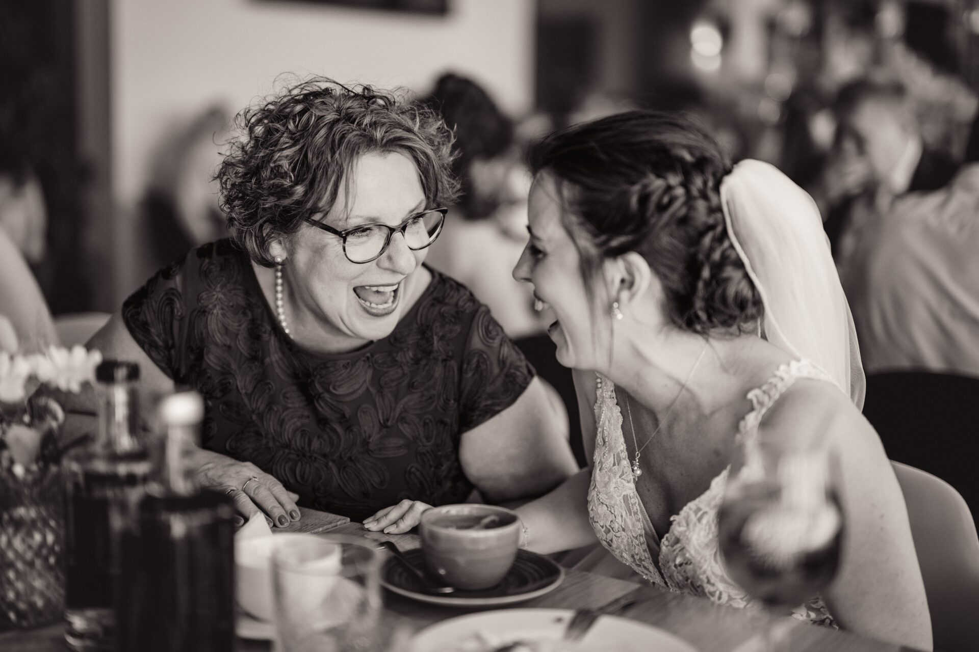 Eine Braut und ein Bräutigam stehen in einer Türöffnung, umarmen sich und lächeln sich an. Aufgenommen von einem Hochzeitsfotografen in München, hält die Braut einen Blumenstrauß, und beide sind in Hochzeitskleidung, schön eingerahmt durch ein dekoratives Tor im Freien. Hochzeitsfotos_Hochzeitsfotograf_München