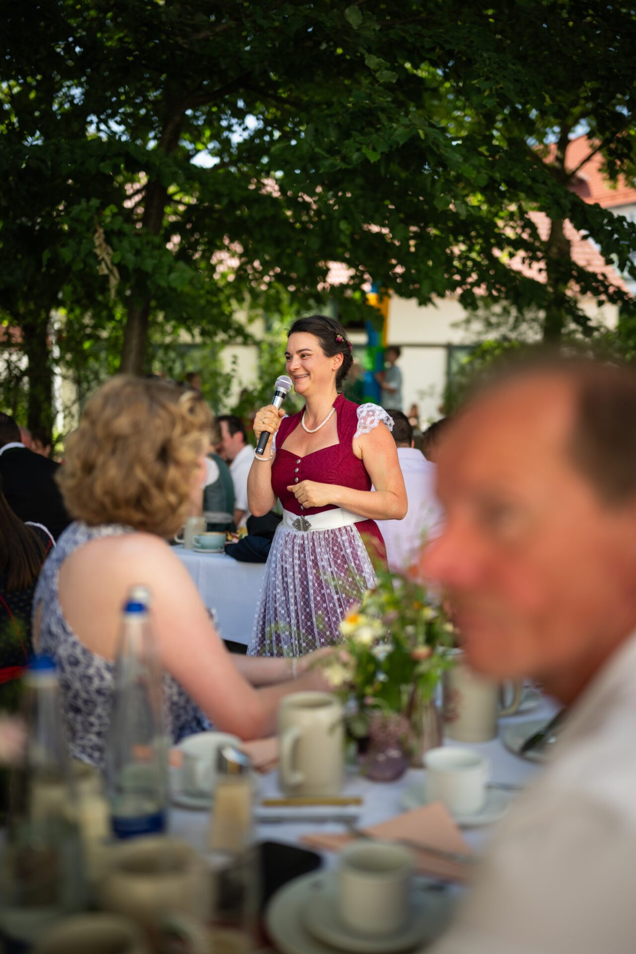 Ein Mann im Anzug umarmt eine lächelnde Frau in einem geblümten Kleid. Sie stehen dicht beieinander vor einer Holzwand und teilen einen fröhlichen und intimen Moment – perfekt für unvergessliche Hochzeitsfotos vom Hochzeitsfotograf aus München. Das Foto ist in schwarz-weiß gehalten. Hochzeitsfotos_Hochzeitsfotograf_München