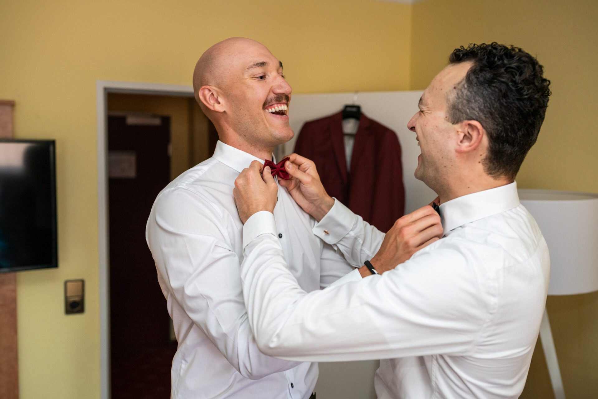 Drei förmlich gekleidete Personen, zwei Männer in blauen Anzügen und eine Frau in einem roten Kleid, stehen lächelnd zusammen vor einem Holzzaun – perfekt für Hochzeitsfotos von einem Hochzeitsfotografen in München. Hochzeitsfotos_Hochzeitsfotograf_München